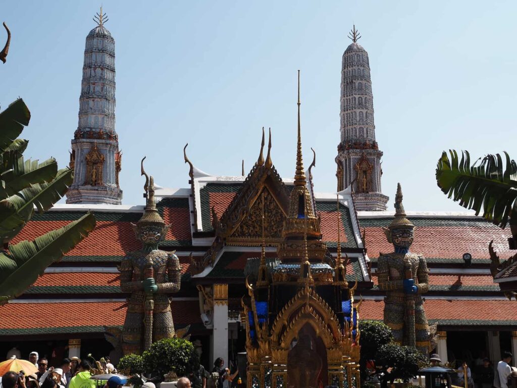 Wejście do świątyni z olbrzymami strażnikami i białymi wieżami w tle w kompleksie Wat Phra Kaew.